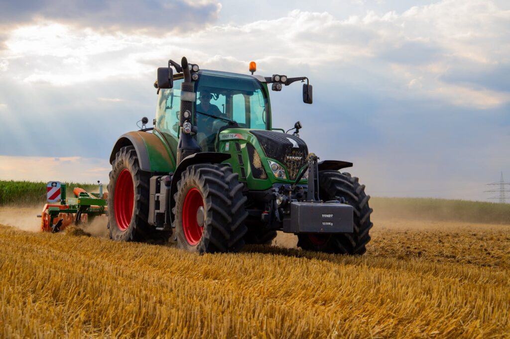 pexels-photo-2933243 A powerful green tractor plowing a dusty wheat field under a cloudy summer sky in rural Germany.